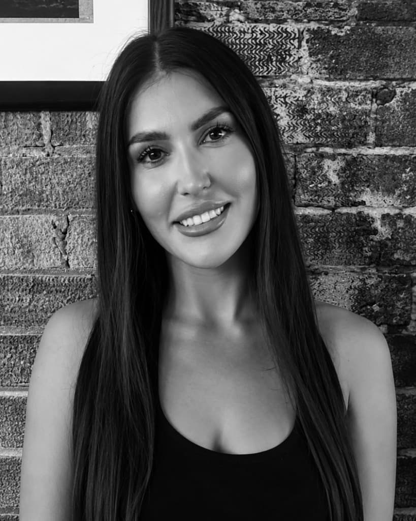 Black and white portrait of Marianne, founder of Reset Pilates, smiling in front of a brick wall.